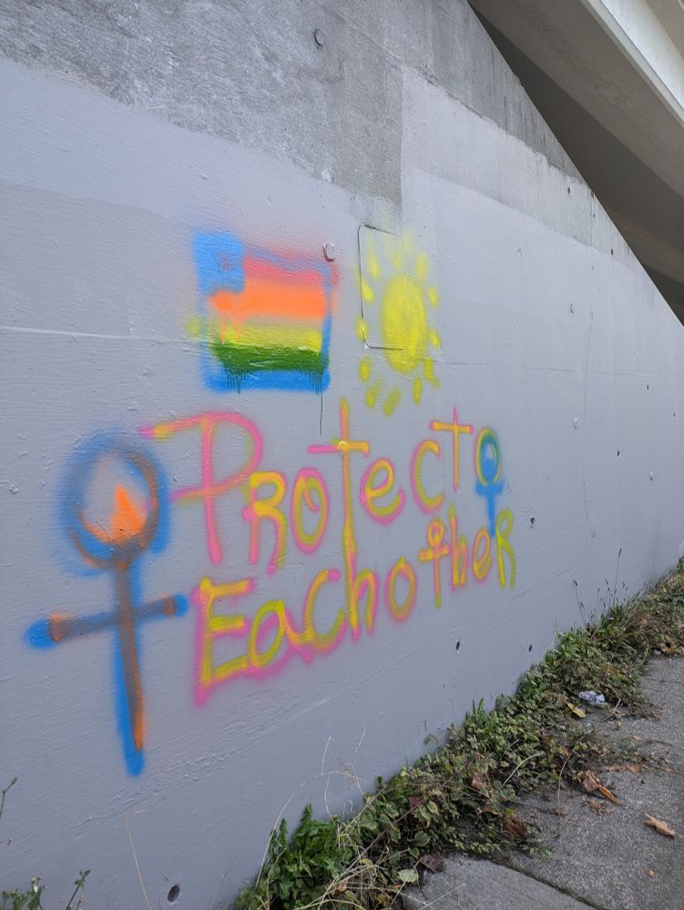 Graffiti that reads "protect each other" with a rainbow flag and sun
