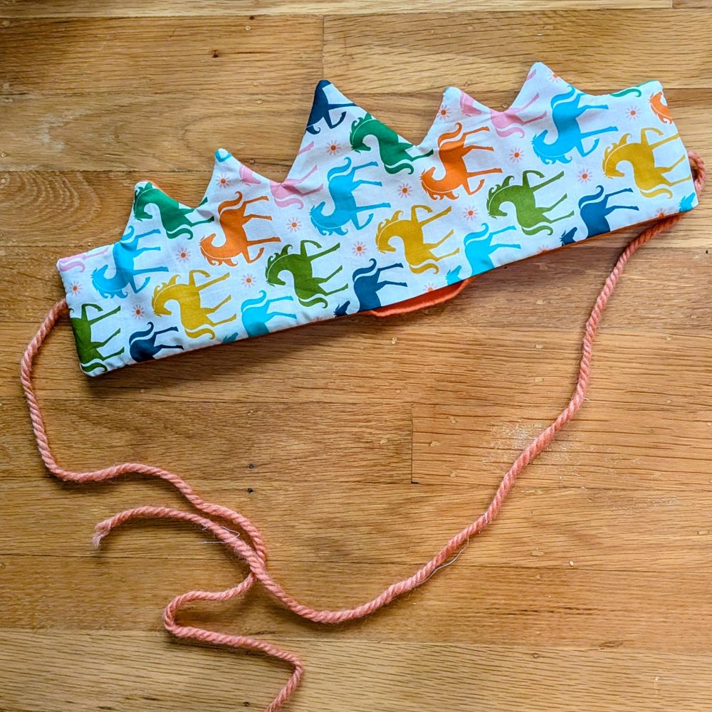 A photo of a fabric crown made out of rainbow horse patterned fabric 