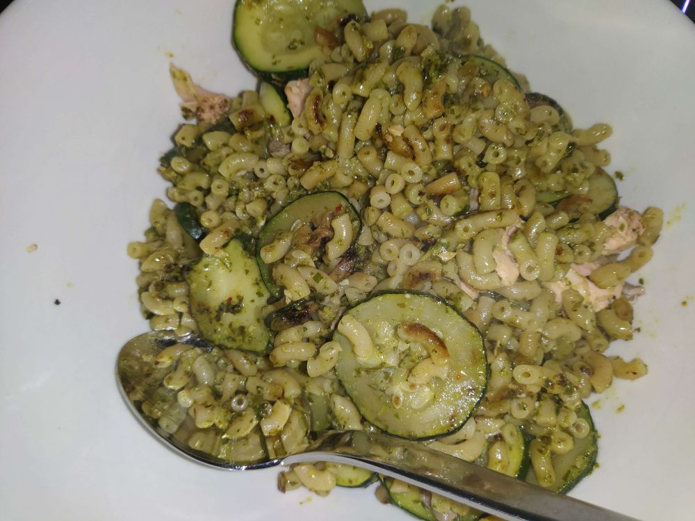Photo of a white bowl with food. Macoroni, fried courgette (zucchini), pesto and salmon.
