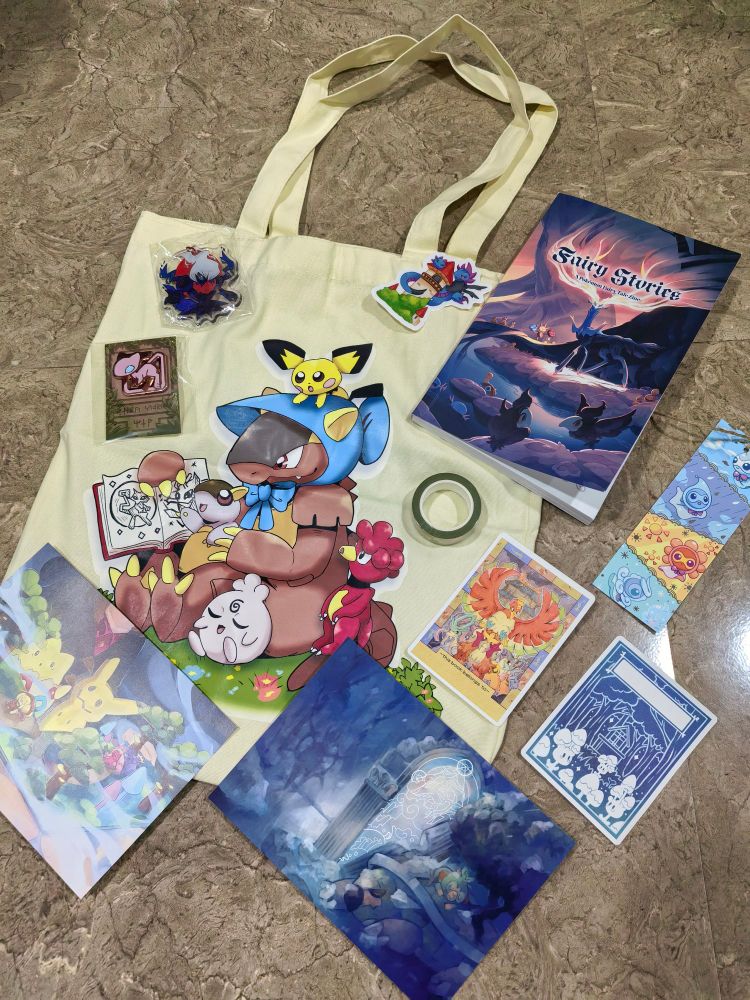 The photo shows a tote bag, washi tape, two prints, a bookmark, two book plates, a keychain, a pin, a sticker, and zine from the Fairy Stories: a Pokémon Fairy Tale Zine 