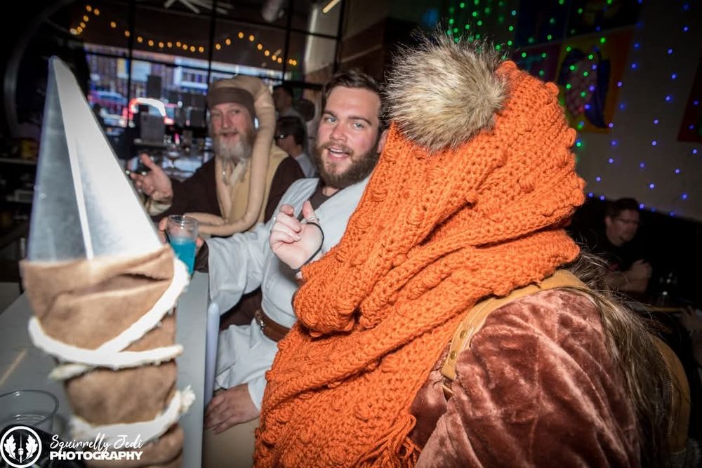 A shot from the side of Wicket (Hannah Solo) with Tony-Wan Kenobi and Twi-Gon Jinn facing her, in conversation while sitting at the bar.