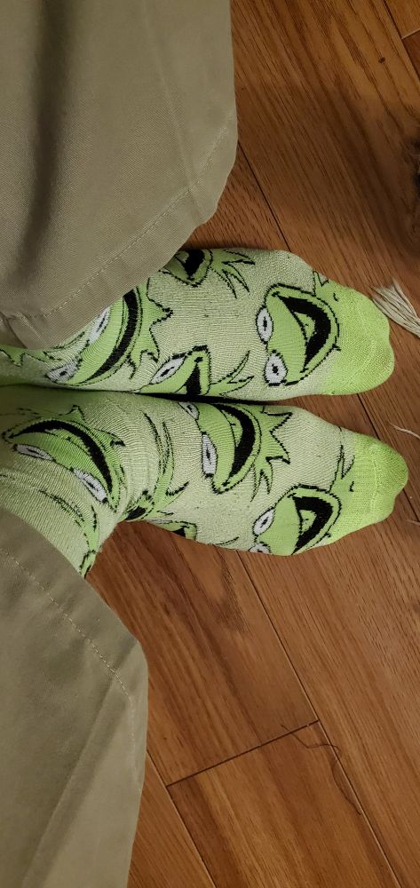 A man's feet. He is wearing Kermit the Frog socks that are, unsurprisingly, green.