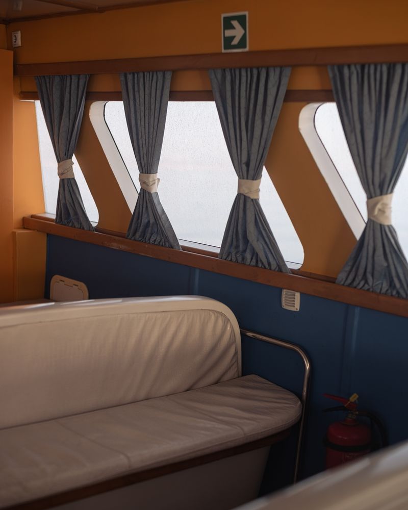 Photograph of part of the seating, window and curtains inside a taxi boat.