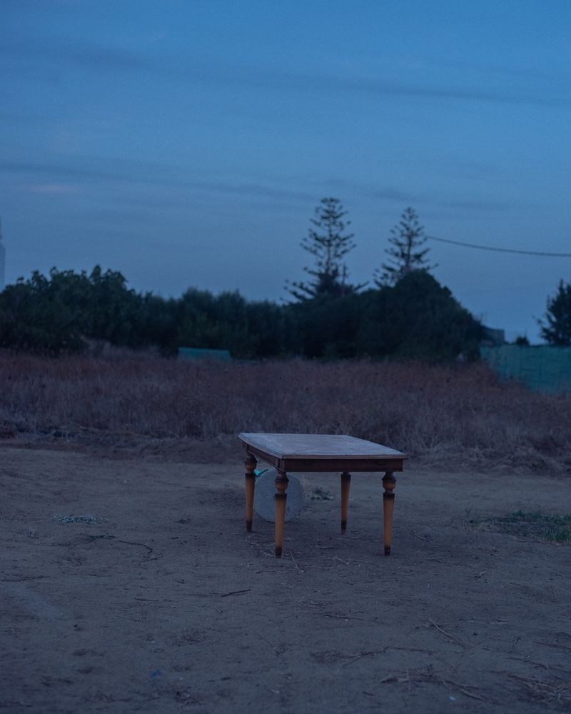 A wooden table photographed in blue hour residual light standing like an out of place artifact in a sparse greek backland surrounding 