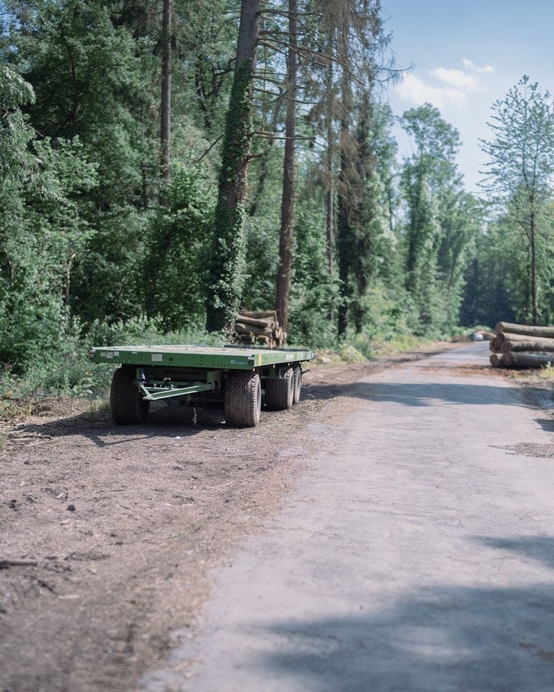 An empty trailer for forest harvesting fruits parked on the side of a dirt road.
