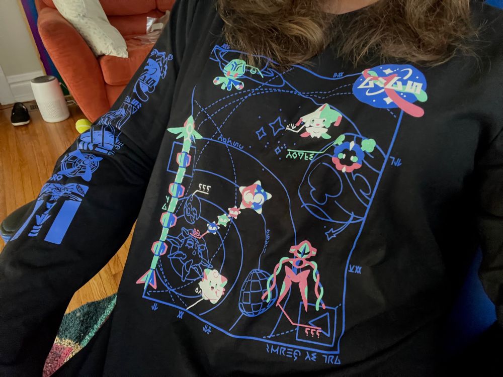 close up of shirt, black long sleeve with pastel art of different space pokémon