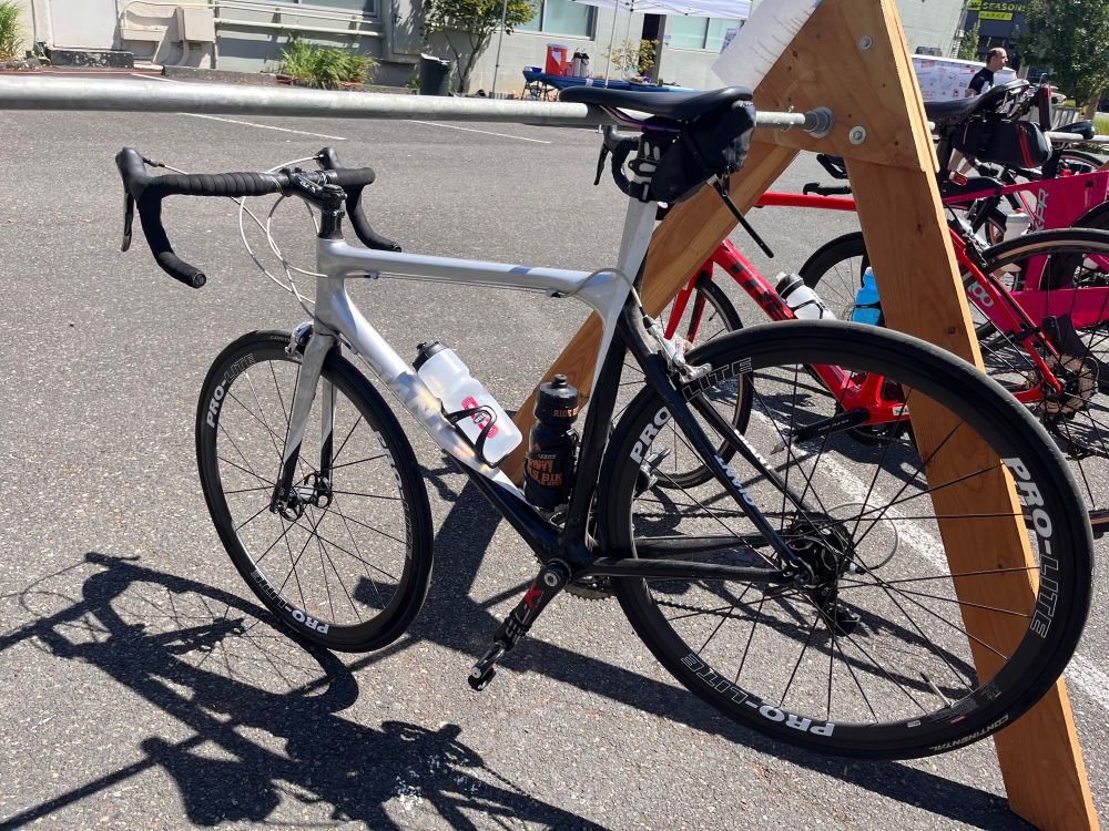 A silver and black giant TCR on the same bike stand from the first pic but now it’s sunnier out 