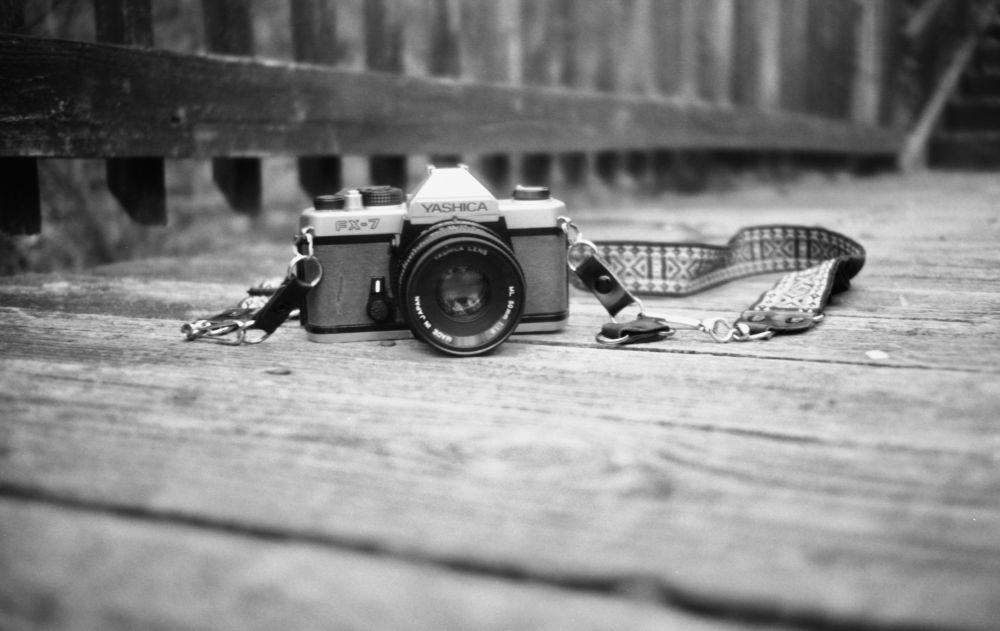 Yashica FX-7 w/50mm lens and strap resting on a wooden stairwell. Photo is taken at ground level. 