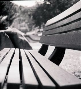 Close-up of a park bench in black and white with large rocks in the background 