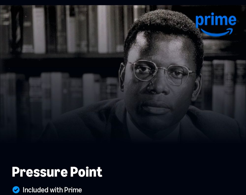 Screenshot of the movie from Amazon Prime Videos. Showing Sidney Poitiers with round rim glasses, a library in the back