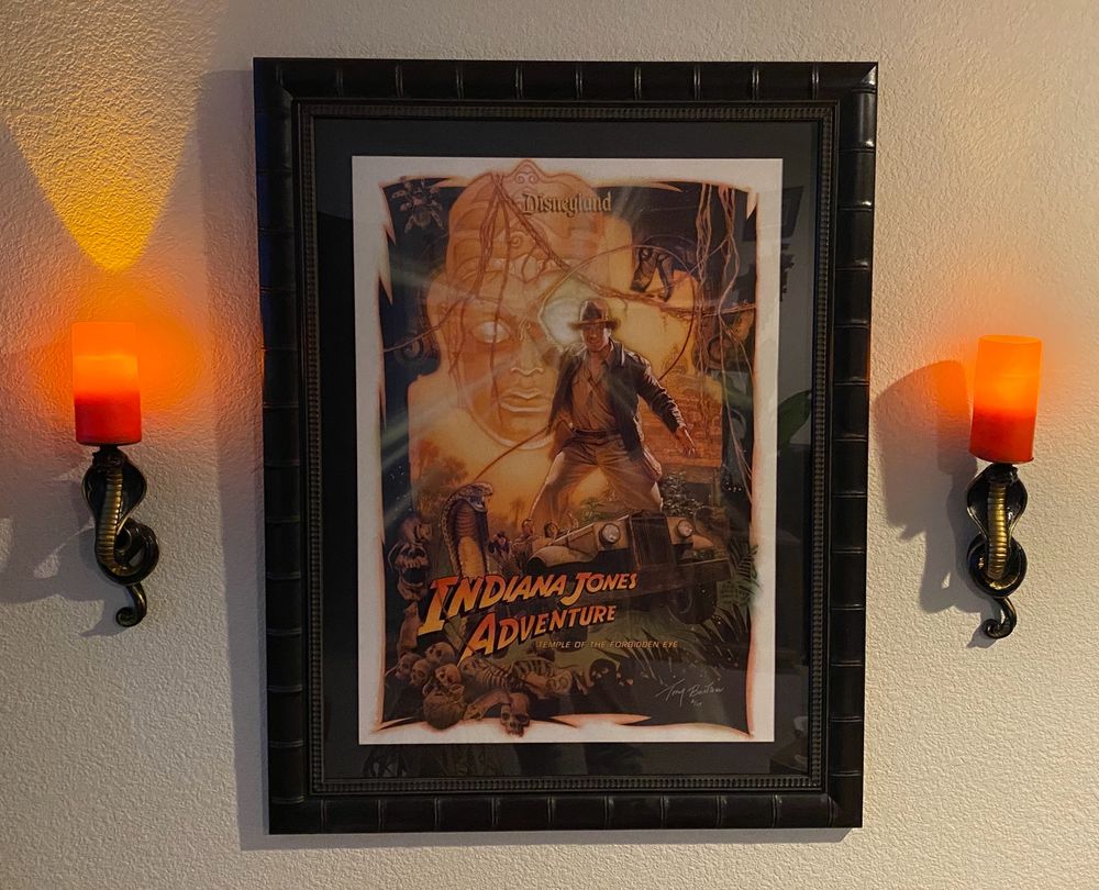Framed Indiana Jones Adventure attraction poster, surrounded by snake sconces with glowing orange and red candles.