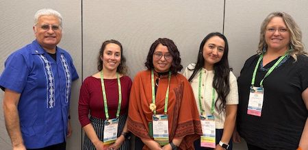 Photo of panelists from &quot;Postdoc Fundamentals&quot; session all standing from left to right Roca, Palominos, Paniagua, Zamora, and Sugiura. Roca is older with gray hair wearing glasses and blue guayabera shirt. Palominos has shoulder-length brown hair and is in a red shirt. Paniagua has shoulder-length brown hair and is wearing glasses and an orange cape-like sweater. Zamora has long brown hair and is wearing a white shirt with buttons. Finally Sugiura has shoulder-length blond hair while wearing glasses and a black blouse.