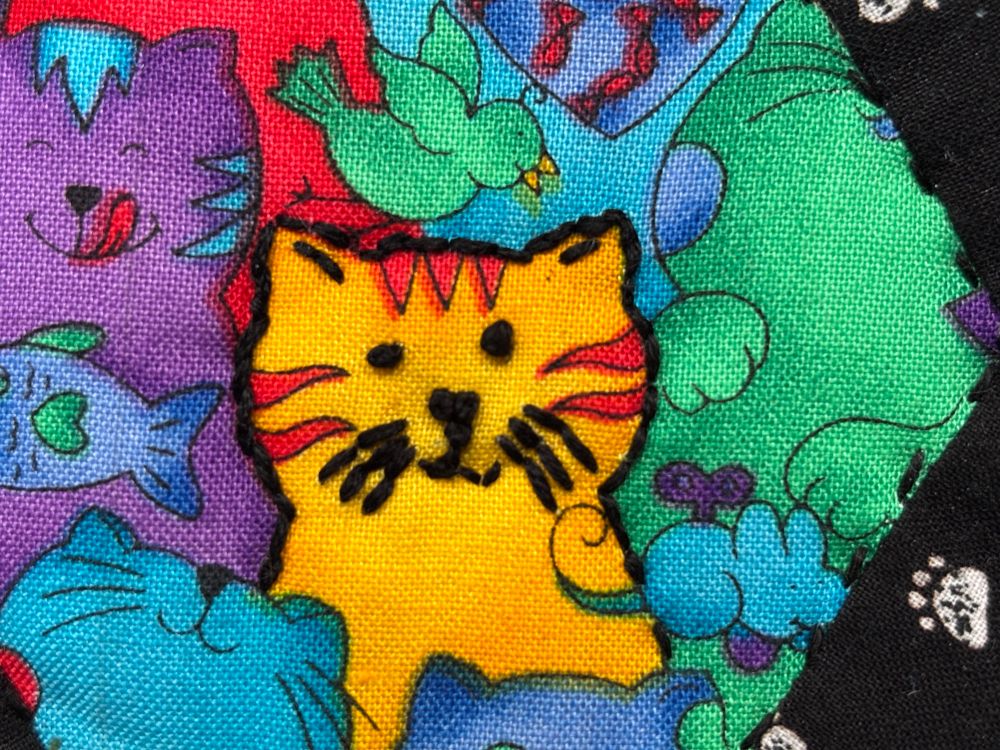 Closeup of the coaster central piece with black stitches reinforcing the outline of a yellow cat
