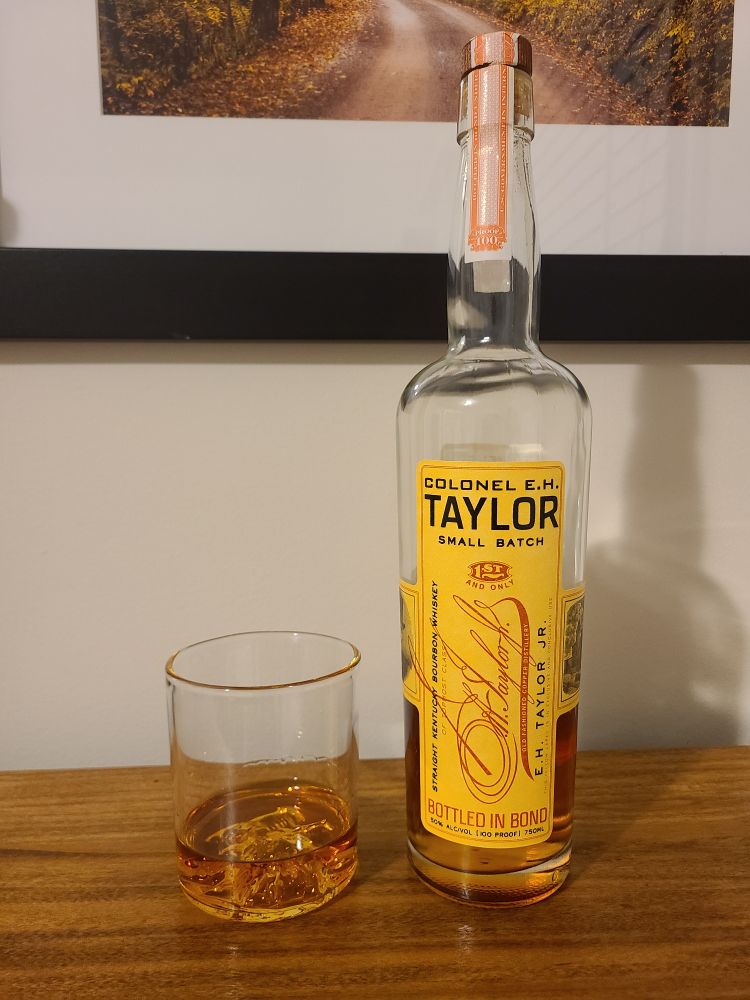 Glass of bourbon sitting next to a bottle of E.H. Taylor bourbon