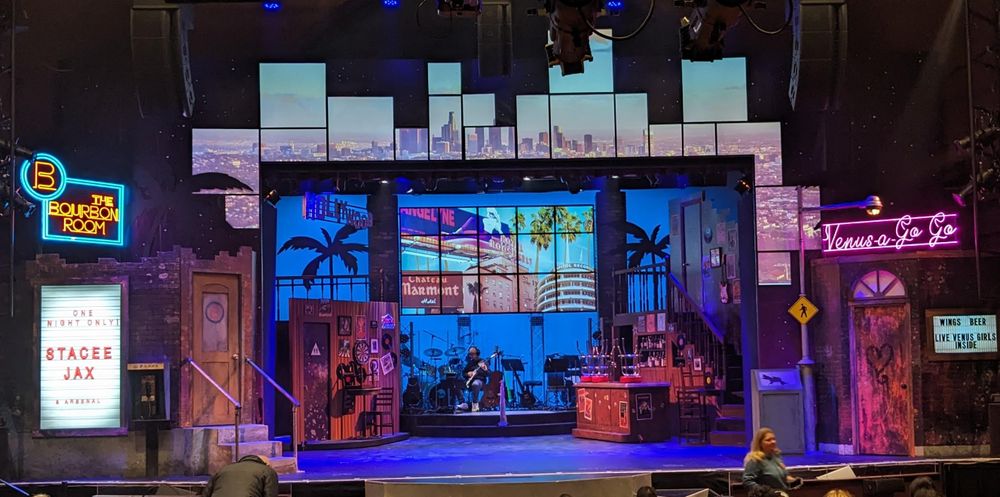 Rock of Ages set: There's a lot going on, displays, bathroom exterior, projections, a band, a bar, neon signs, etc