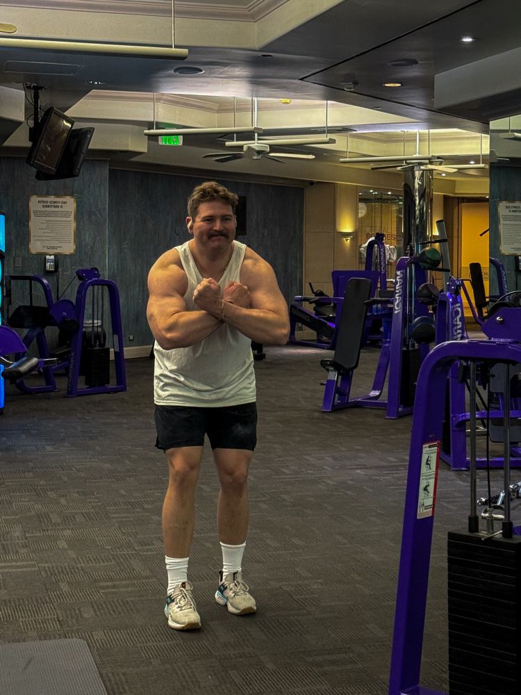 Dude, flexing in gym mirror he is wearing a white tank top, black shorts, white socks, and white shoes