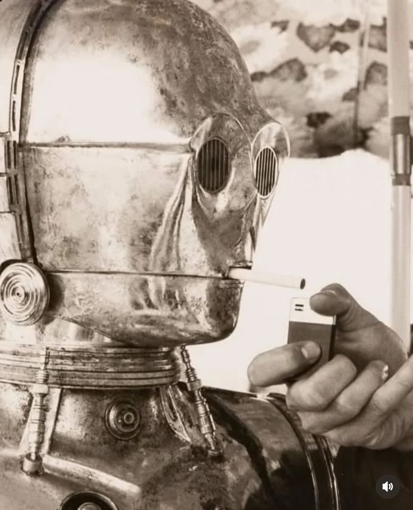 C-3PO with a cigarette in his mouth being lit by and other person. 