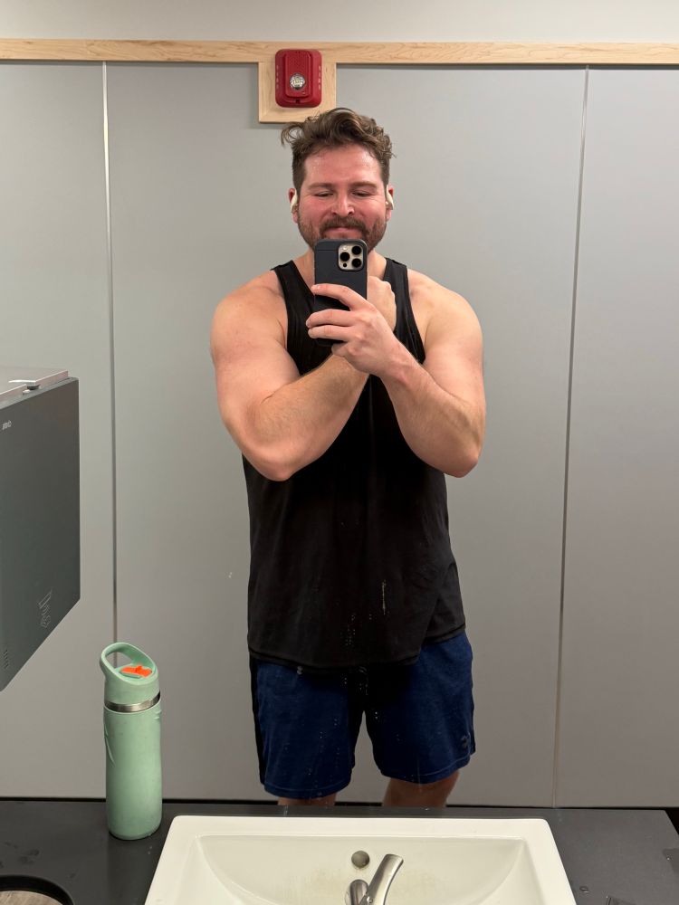 Dude, posing in mirror with black tank top and blue shorts posing in mirror boxing muscles