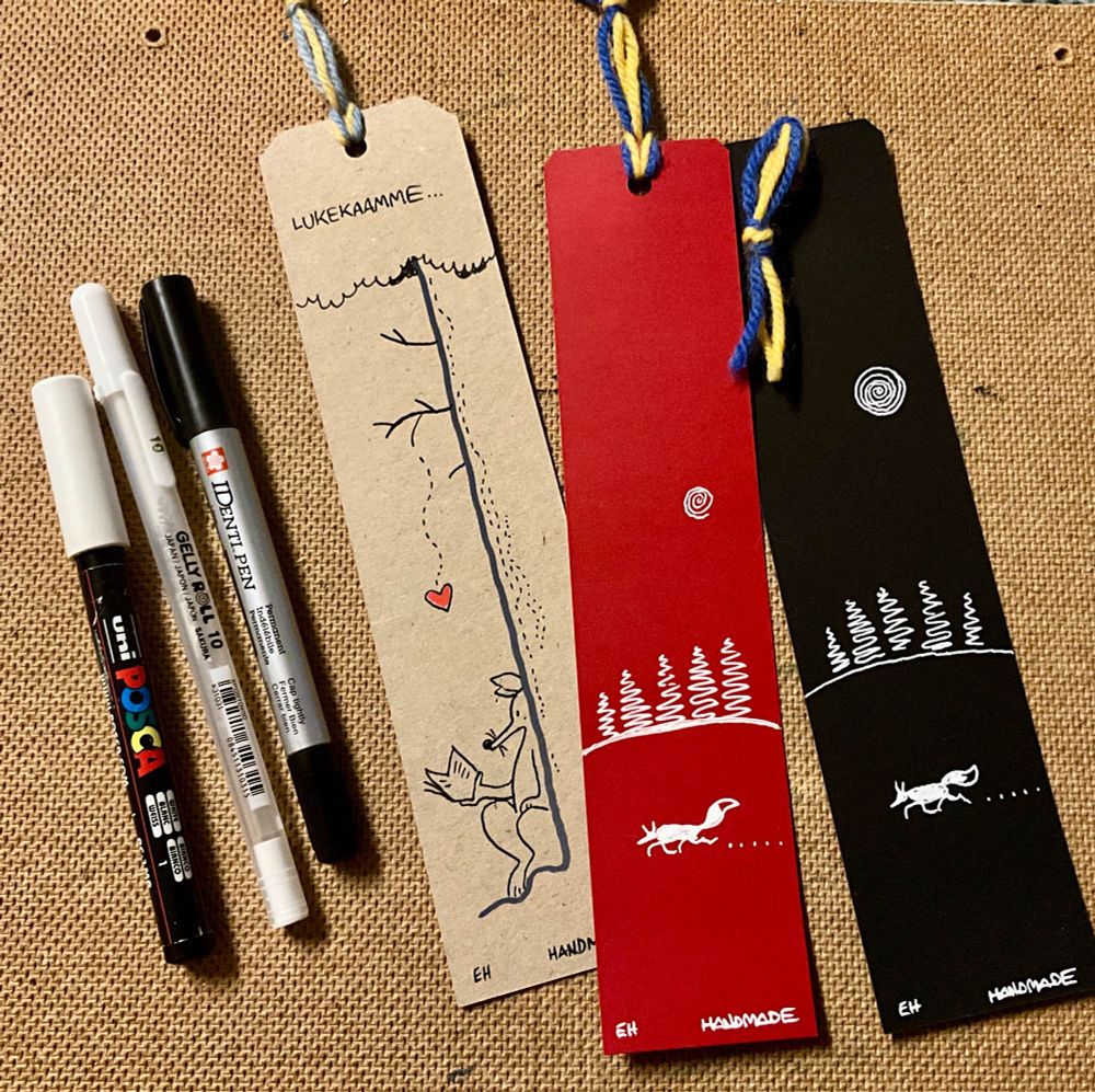 Kolme käsinpiirrettyä kirjanmerkkiä, hapsut Ukrainan väreissä. Kuvassa myös tuotantovälineet