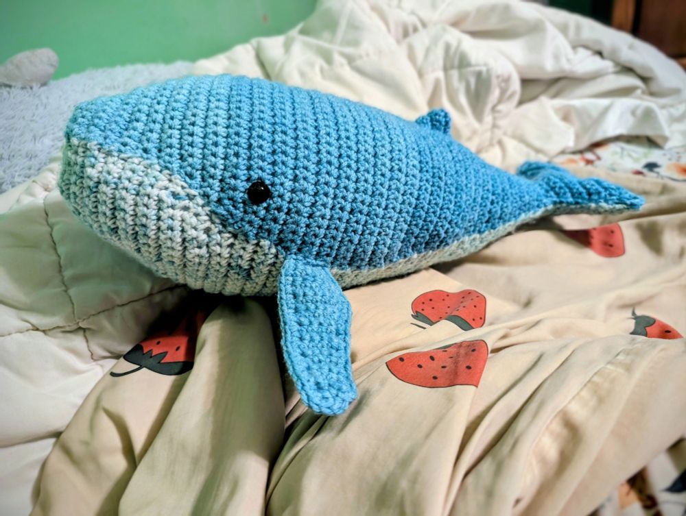 a crochet humpback whale sitting on some blankets 