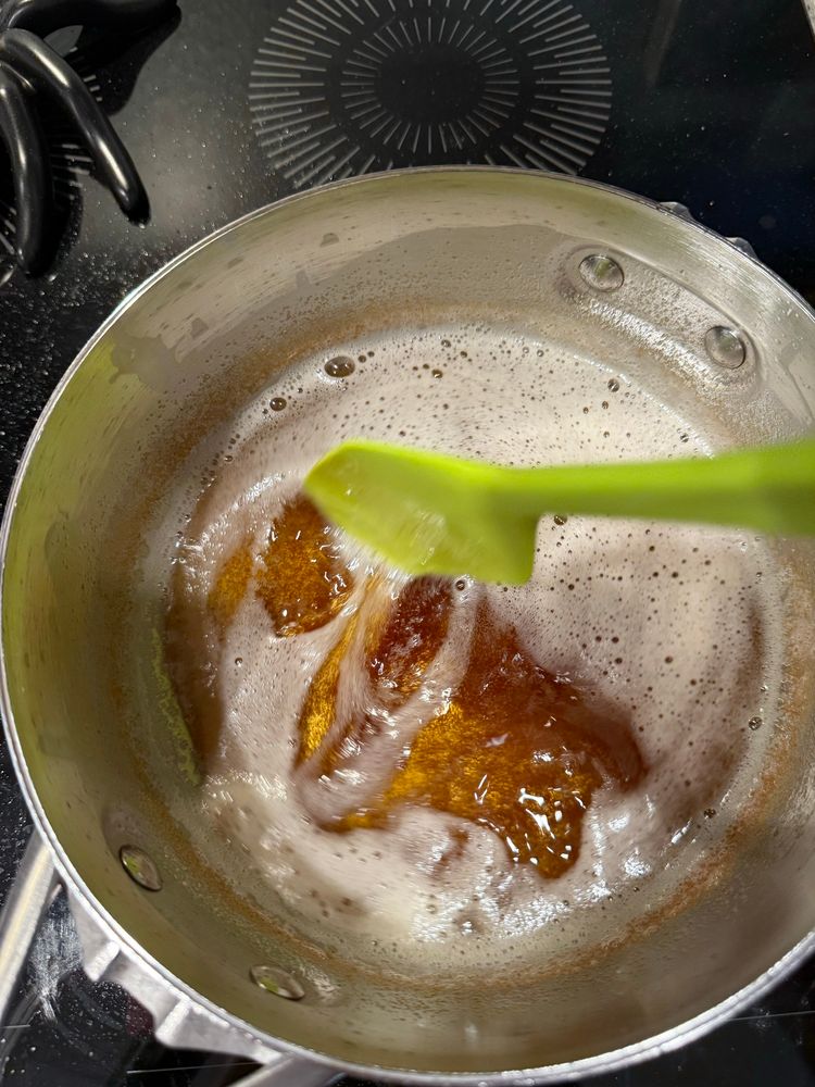 A green spatula stirs foamy browned butter. 
