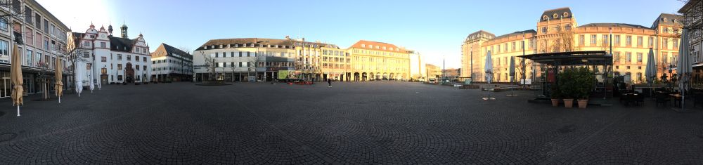 A panoramic photo of a place that is (nearly) completely empty. One person walking along.
The morning sun shines on some buildings.