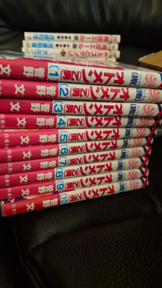 a stack of all 10 volumes of Otomen on a black leather couch, in the background there are more manga