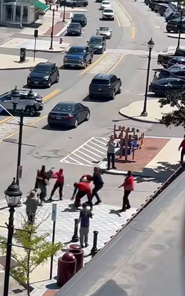 nazi dorks in a fight with a bystander down on a street. hard to make out details but it's blood tribe in matching red uniforms.