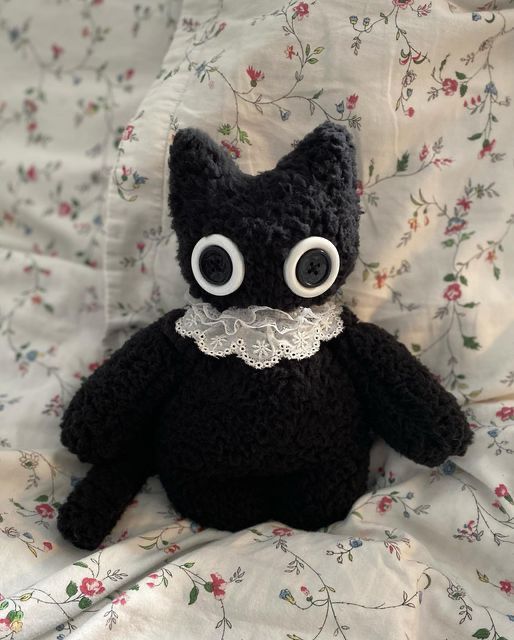 a plushie of a black cat with big white eyes and a white frill around its neck