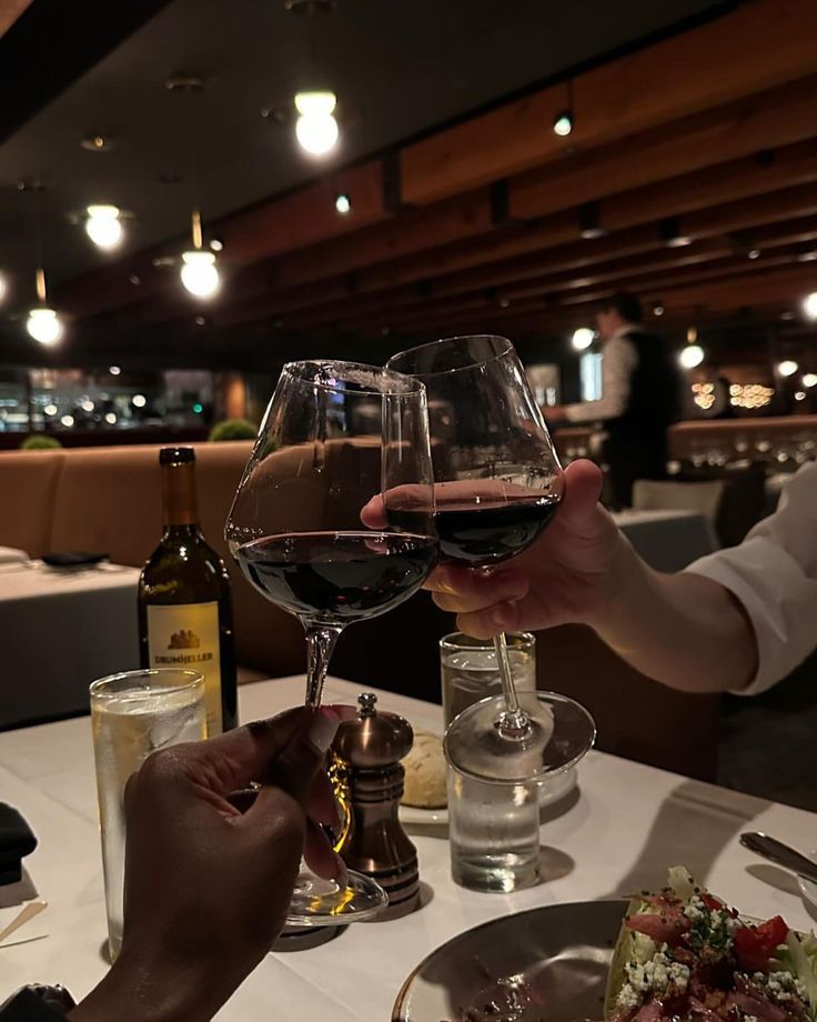 two people clinking wine glasses in a dim restaurant
