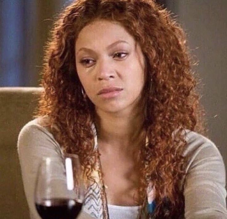 a woman sitting in front of a glass of wine, looking off into space with a tired expression and tears under her eyes