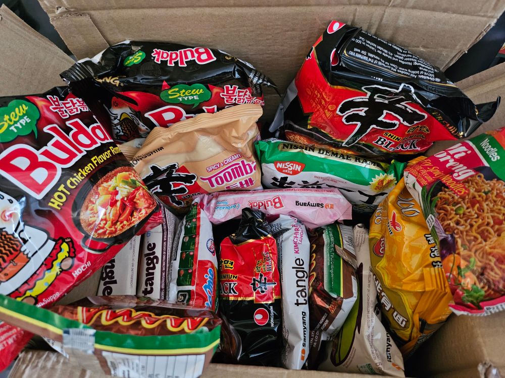 A box full of instant ramen/pasta:

-2x Indomie Mi Goreng stir-fry spicy noodles
-2x Mama Pa-Lo Duck noodles
-2x Nissin Kyushu Tonkotsu noodles
-2x Shin Black
-2x Shin Toomba
-1x Buldak Carbonara
-2x Buldak stew type
-1x Samyang Tangle creamy bulgogi 
-1x Samyang Tangle creamy mushroom
-1x Samyang Tangle garlic oil
-1x Samyang Tangle kimchi rose
-1x Unif 100 stewed pork chop noodles