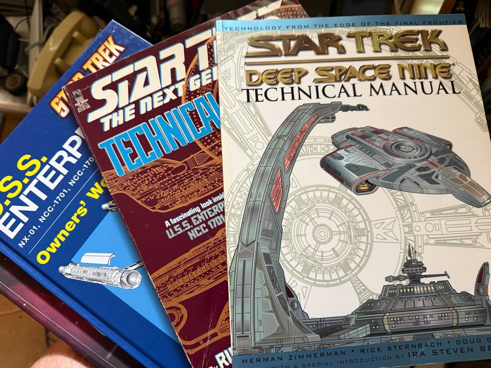 A stack of Star Trek “Technical Manuals” for Deep Space Nine, The Next Generation, and a Hayes manual for the USS Enterprise
