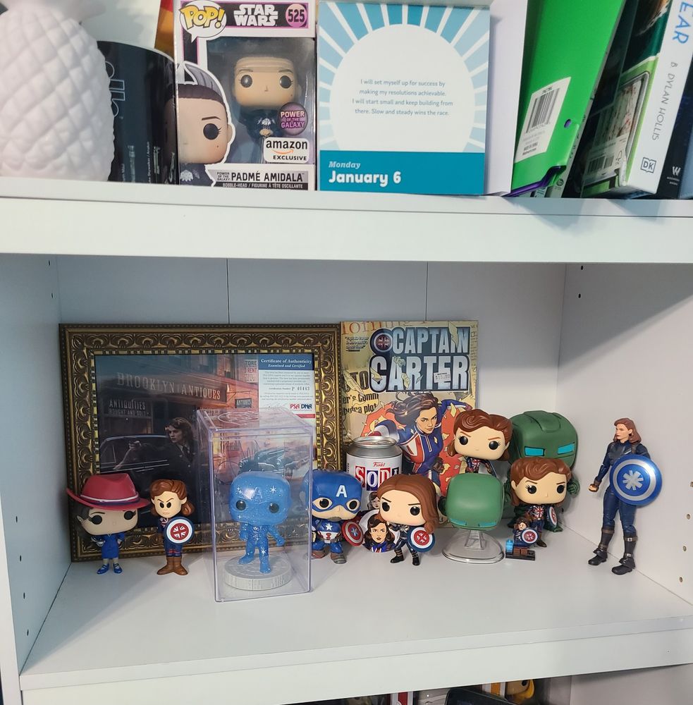 Bookshelf full of funko pops of Peggy Carter and Steve Rogers, with a framed autographed picture of Hayley Atwell and a Captain Carter comic book as well as other figures 