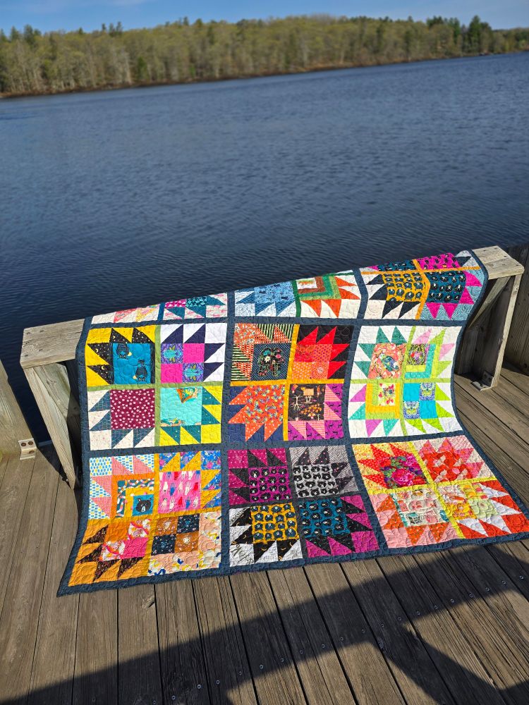 Colorful quilt comprised of Bear Paw blocks set in groups of four with thin sashing between the blocks and a wider border between the groups.
