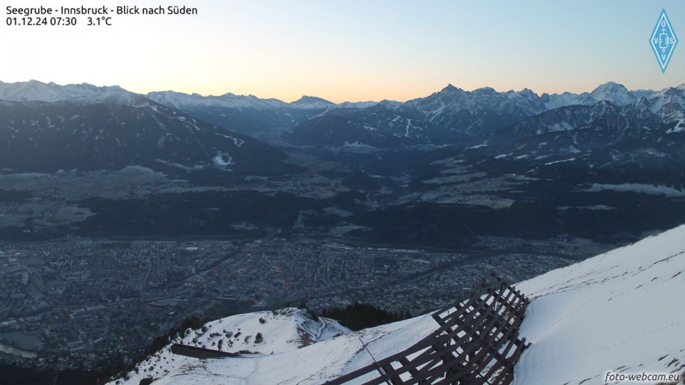 Blick von der verschneiten Seegrube bei + 3,1 Grad über das kalte Innsbruck (- 4,7 Grad). Im Hintergrund sieht man viele Berge und einen rosafarbenen Himmel.