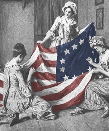 Three women in colonial-era clothing sit indoors, hand-sewing an early U.S. flag with 13 stars in a circle; the flag is in color (red, white, and blue) while the rest of the image is grayscale.
