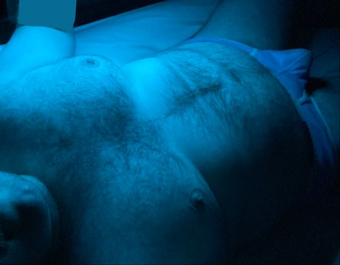 A picture of me laying in bed bathed in blue light. 
I'm only wearing a pair of Aussiebum briefs and showing off my chubby hairy body