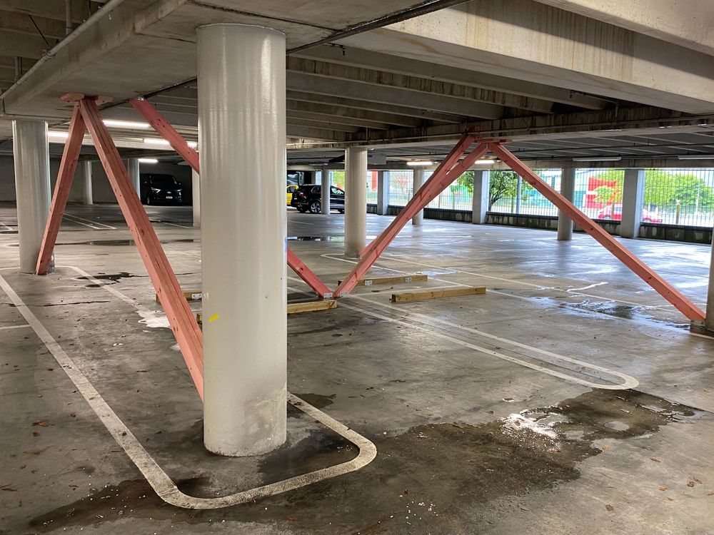 The picture shows an underground carpark with concrete posts, ceiling and floor, but propped up with fresh pink timber bracing