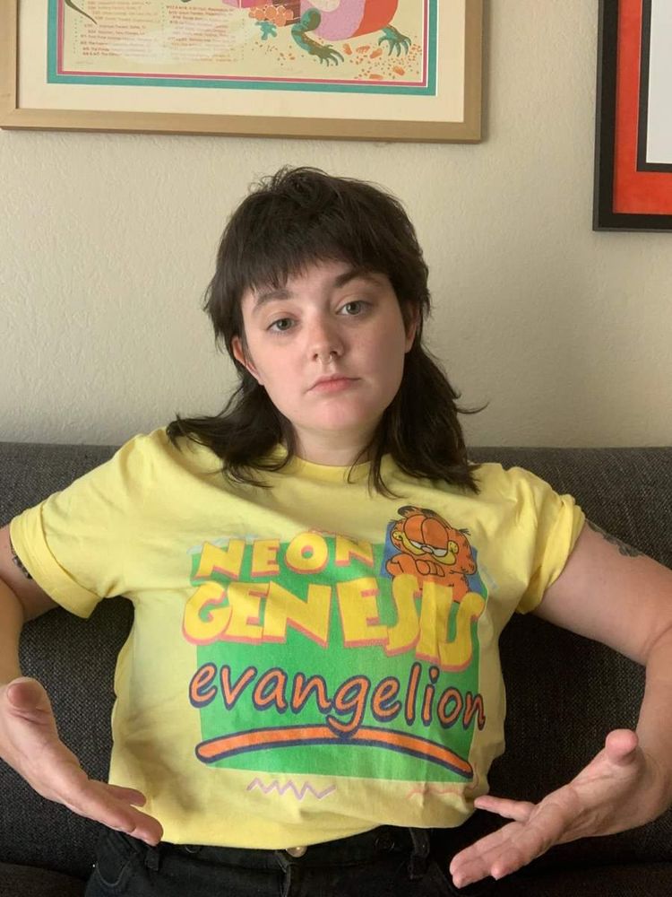 Photo: A young woman wearing a yellow T-shirt; the shirt features the cartoon cat Garfield, as well as a Garfield comic logo that has been modified to read "Neon Genesis Evangelion."