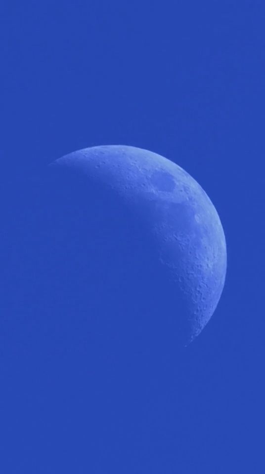 Daylight telephoto of waxing crescent Moon in blue sky.
