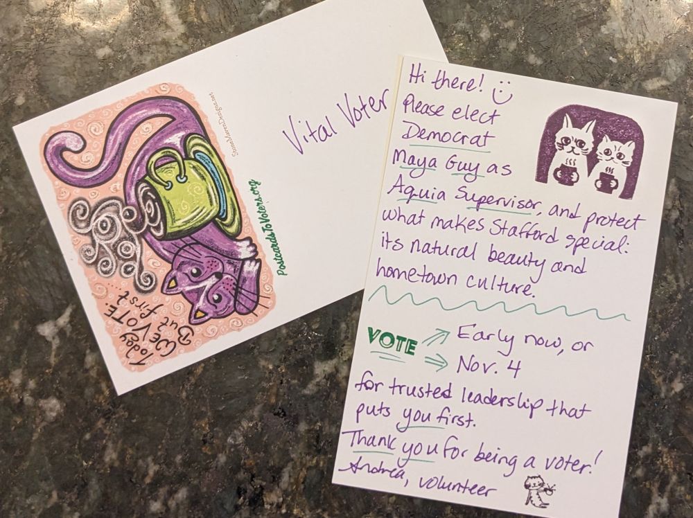 Two postcards laying on a dark surface. One card shows the stamped side with a cartoon drawing of a happy cat curled around a steaming mug of coffee or tea (probably). Text above the cat says "Today we vote. But first...." The second card shows the handwritten side in purple ink saying "Hi there! Please elect Democrat Maya Guy as Aquia Supervisor, and protect what makes Stafford special: its natural beauty and hometown culture. Vote early now or on Nov. 4 for trusted leadership that puts you first. Thank you for being a voter! Andrea, volunteer" There is a cartoon on the right side of two cats sitting next to each other holding mugs with steaming liquid inside.