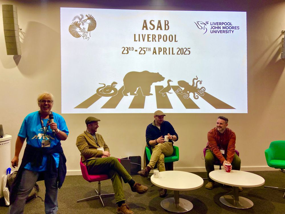 Conference organizer Susi introducing the seated sci comm speakers in front of a slide reading ASAB Liverpool 23rd-25th April 2025