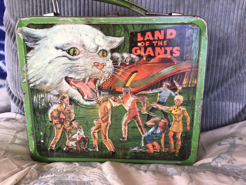 Back side of box. A giant cat menaces the tiny group in front of their craft.

