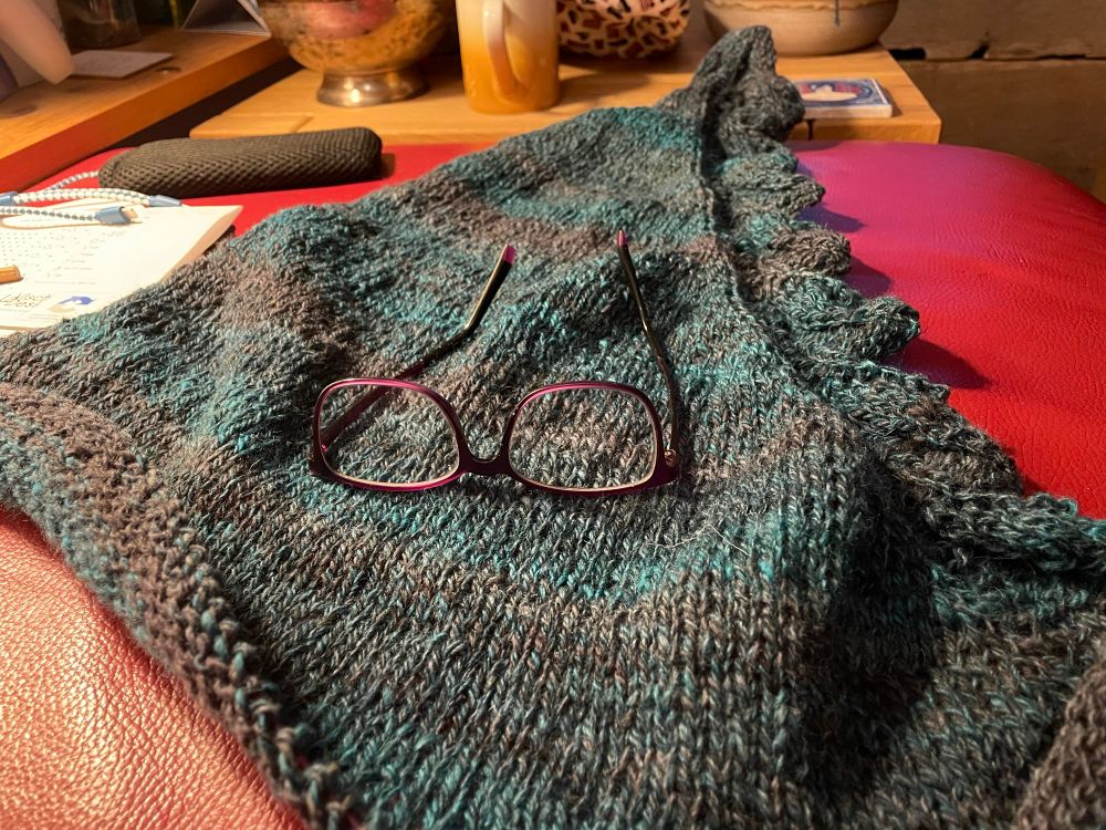 Knitting in progress with a pair of glasses on top. 