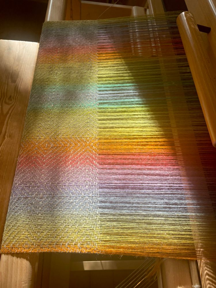 A rainbow coloured warp on a weaving loom, shawl weaving on progress. 