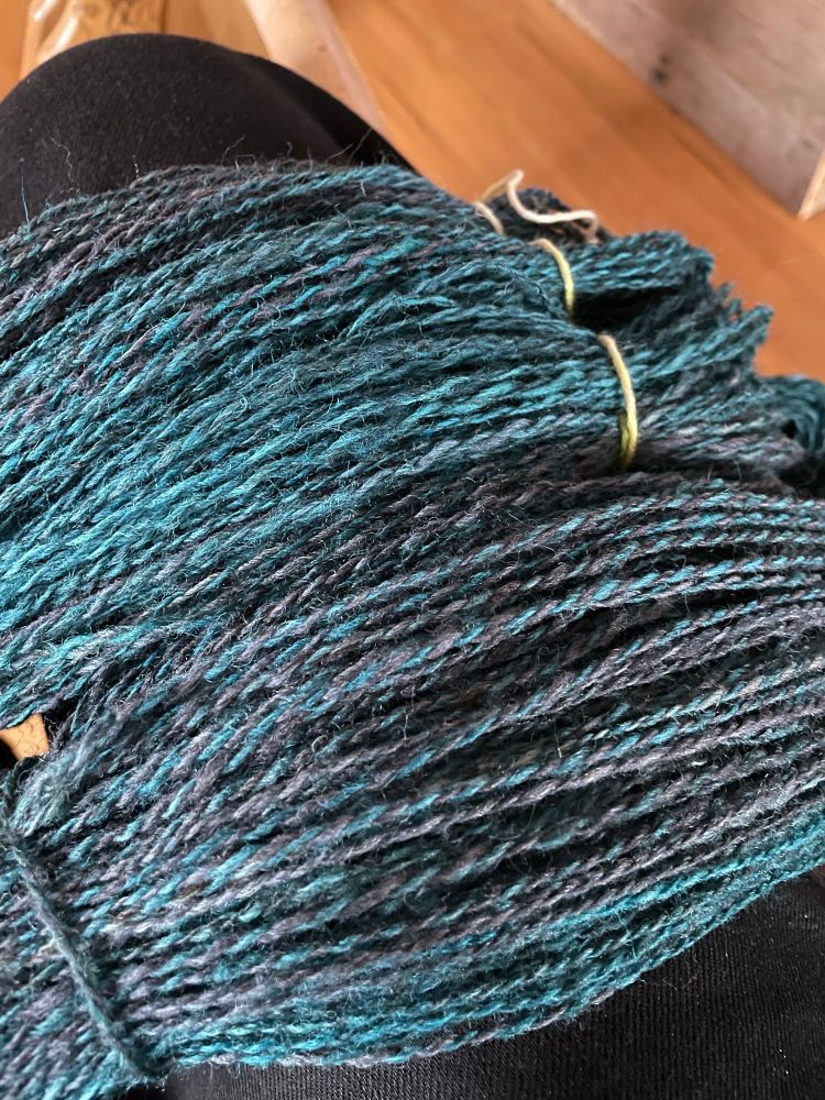Hand spun two-ply yarn , mixed colours of teal and grey. Closeup of the hank. 