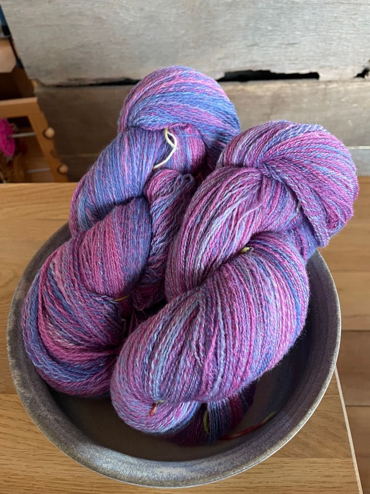 Two skeins of #handspunyarn in a bowl. The colours range from blue to purple and pink. 