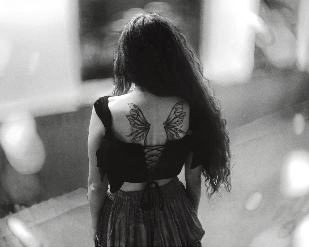 A black and white shot of me from behind in a corset and skirt, showing my fairy wing tattoo off.