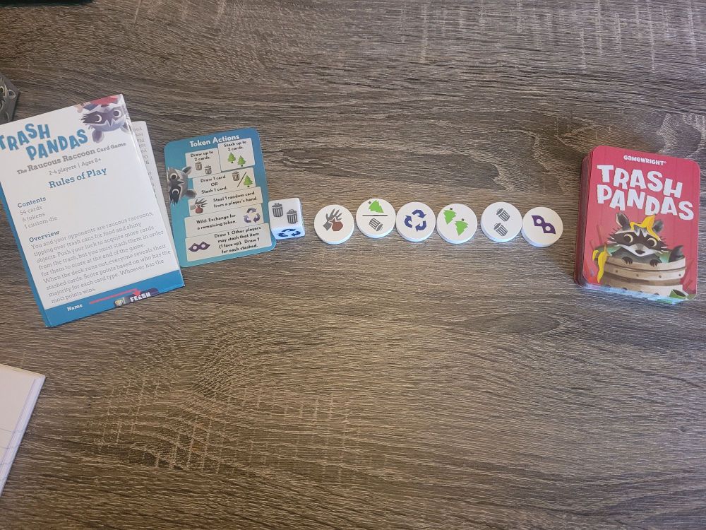 Trash pandas game shown on a table with the instructions, action card, tokens and playing cards